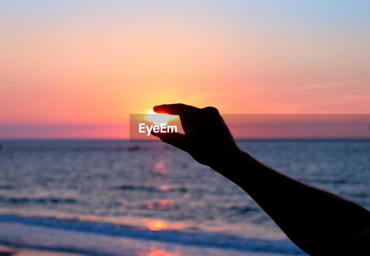 CROPPED IMAGE OF SILHOUETTE PERSON HOLDING SUN AT BEACH