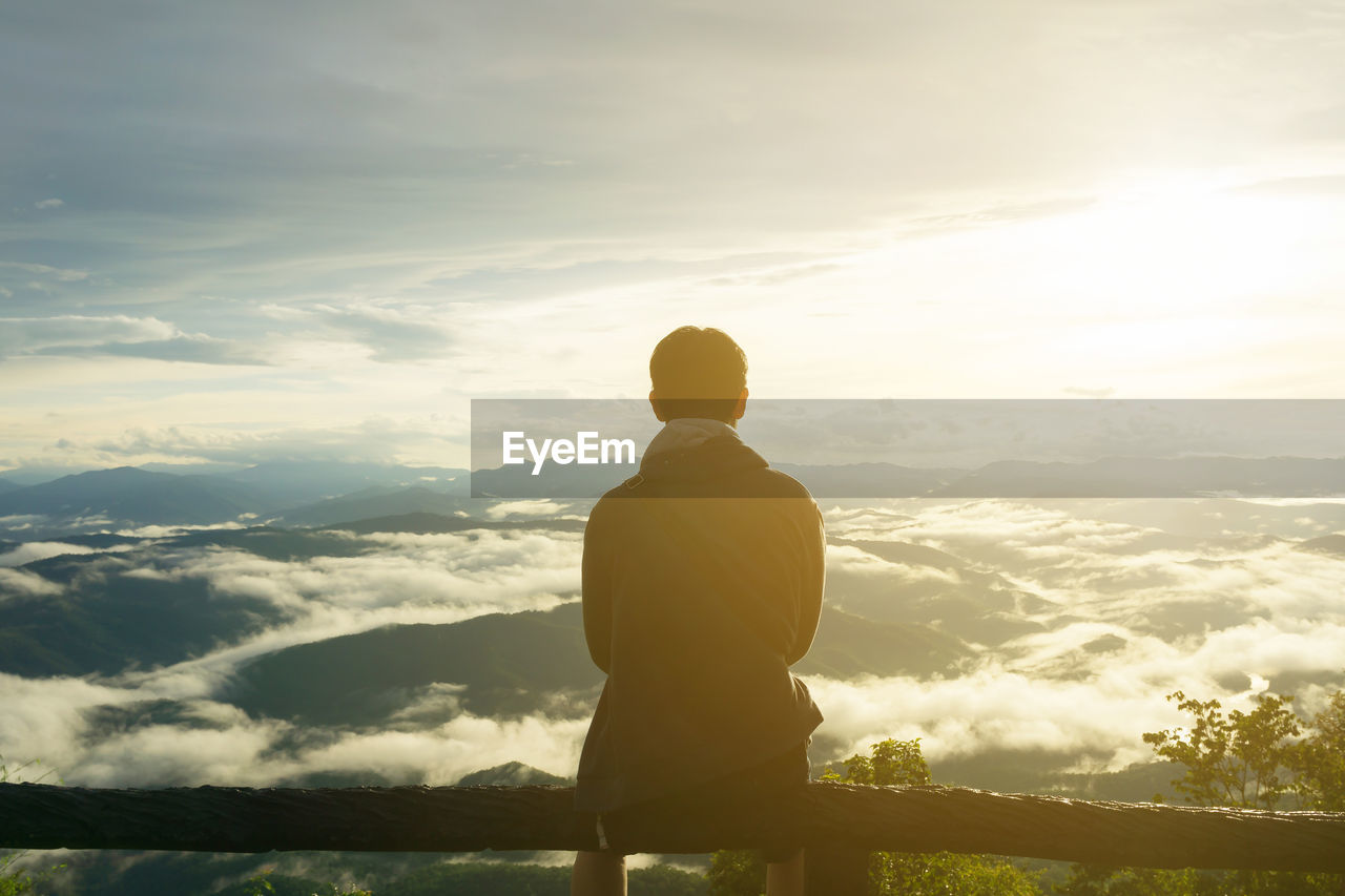 Rear view of man looking at mountain against sky during sunset