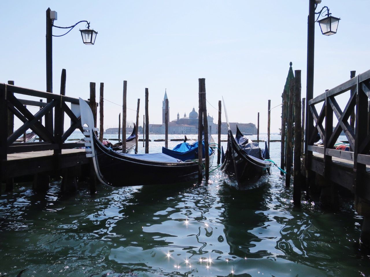 Gondolas moored by pier at venetian lagoon against sky