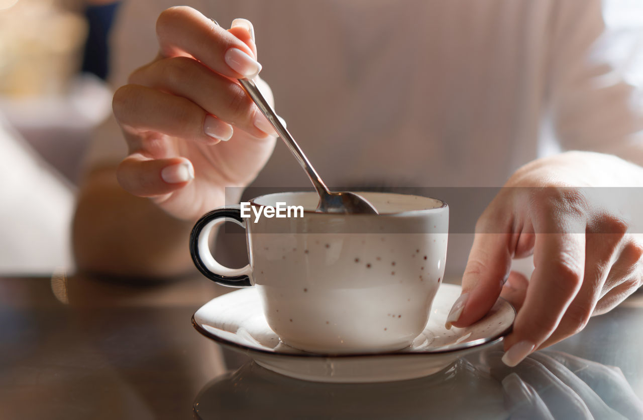 Closeup of female hands with french manicure holding cozy ceramic white mug of tea or coffee