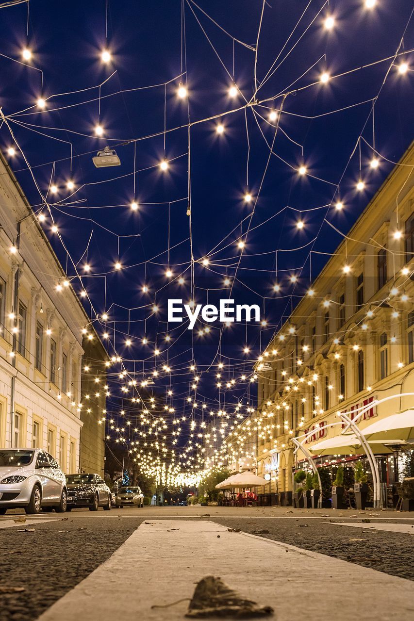 ILLUMINATED STREET AMIDST BUILDINGS IN CITY