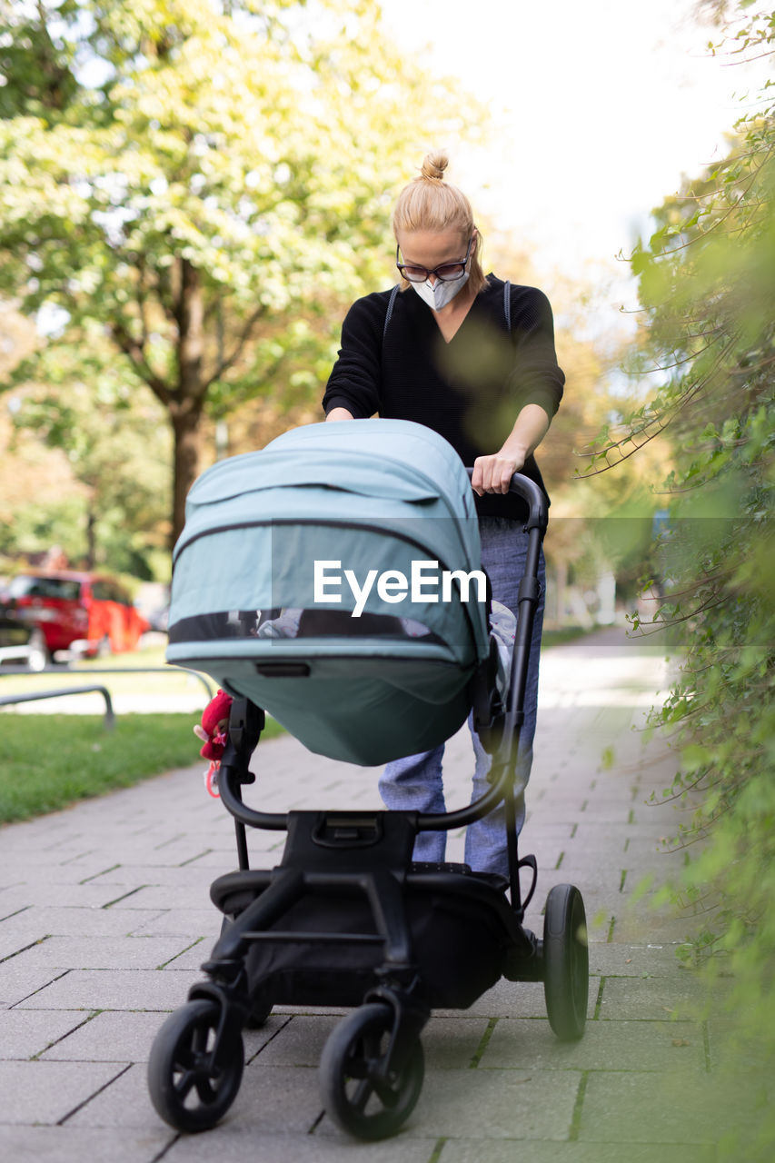 Full length of woman wearing mask with stroller at park