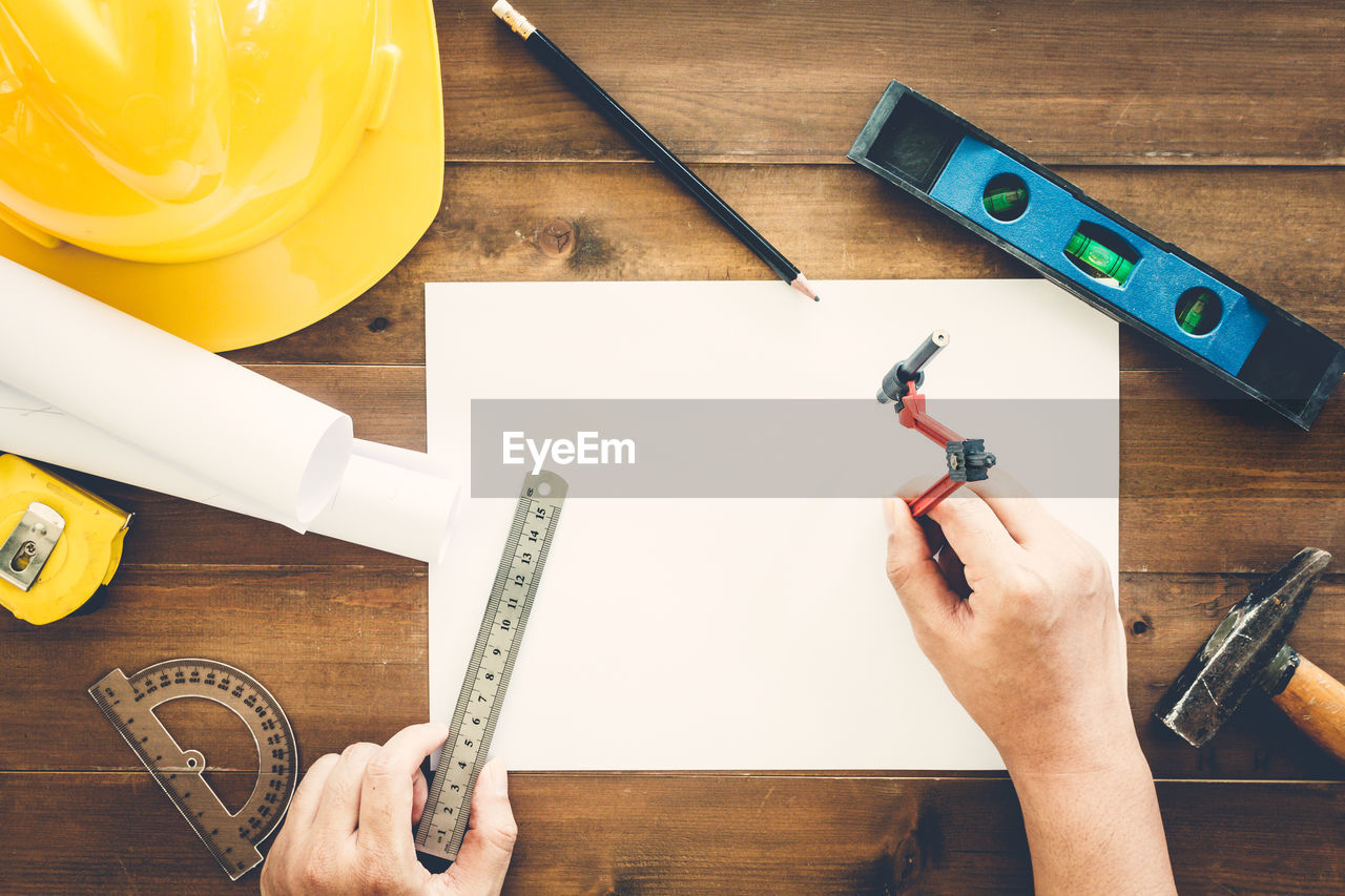 Cropped hands of architect preparing blueprint amidst various tools on wooden table