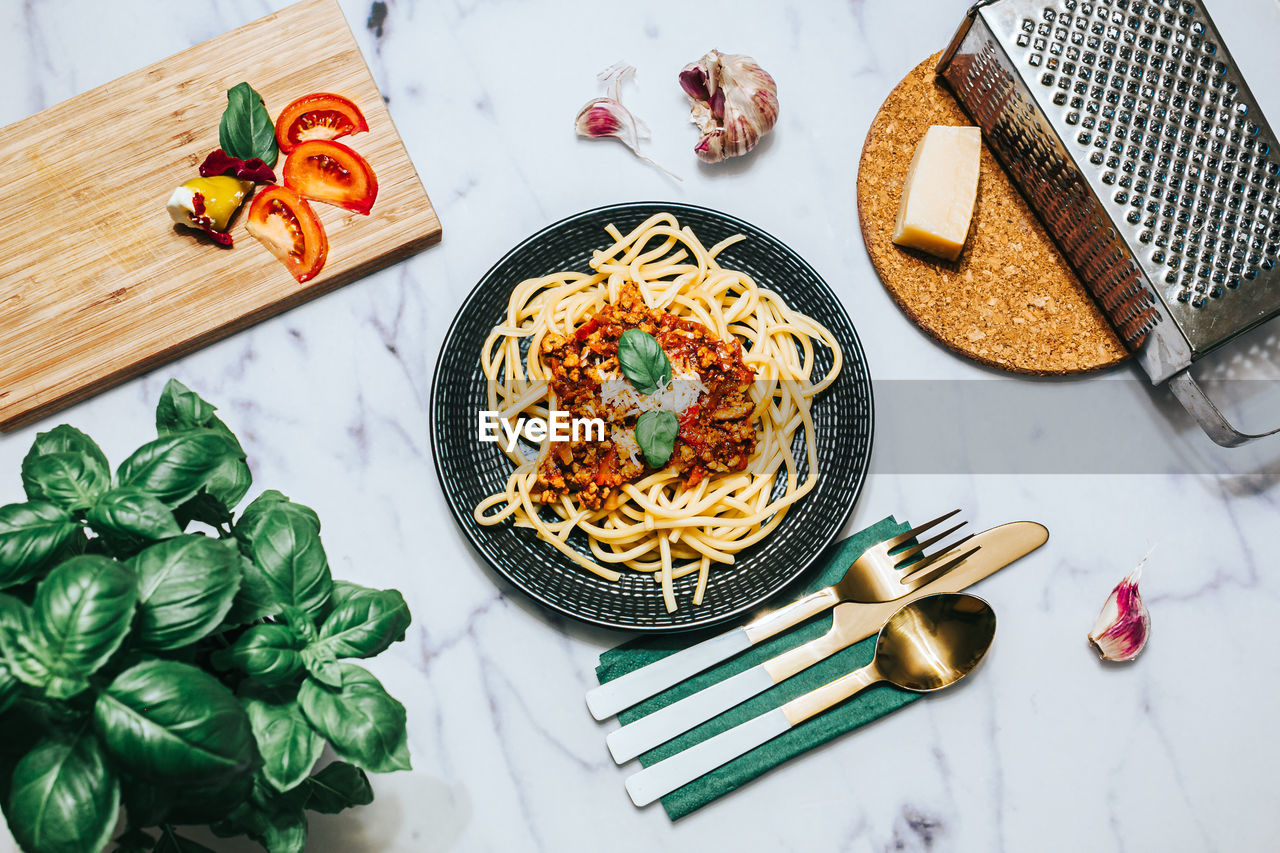 Top view of pasta with bolognese sauce on black plate with eateing utensil and herbs