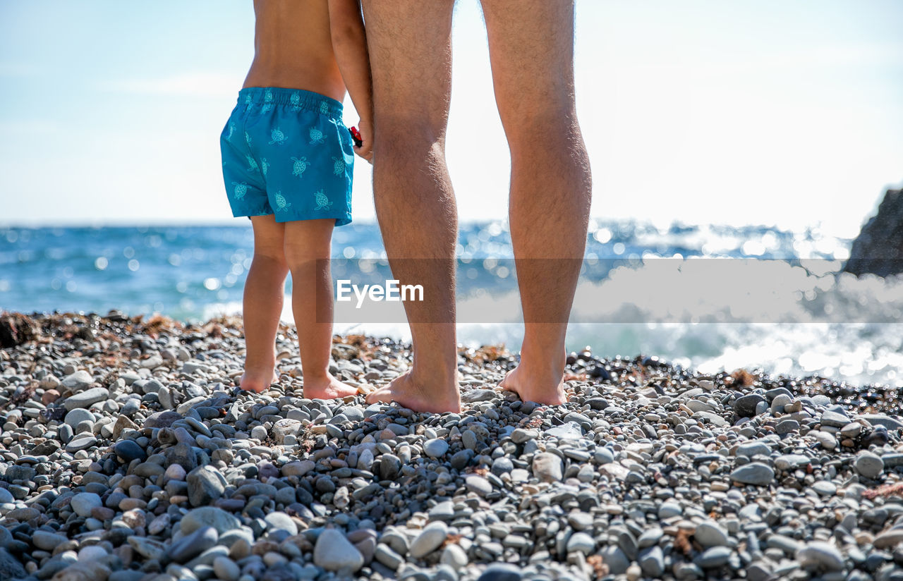 Low section of man with son standing at beach