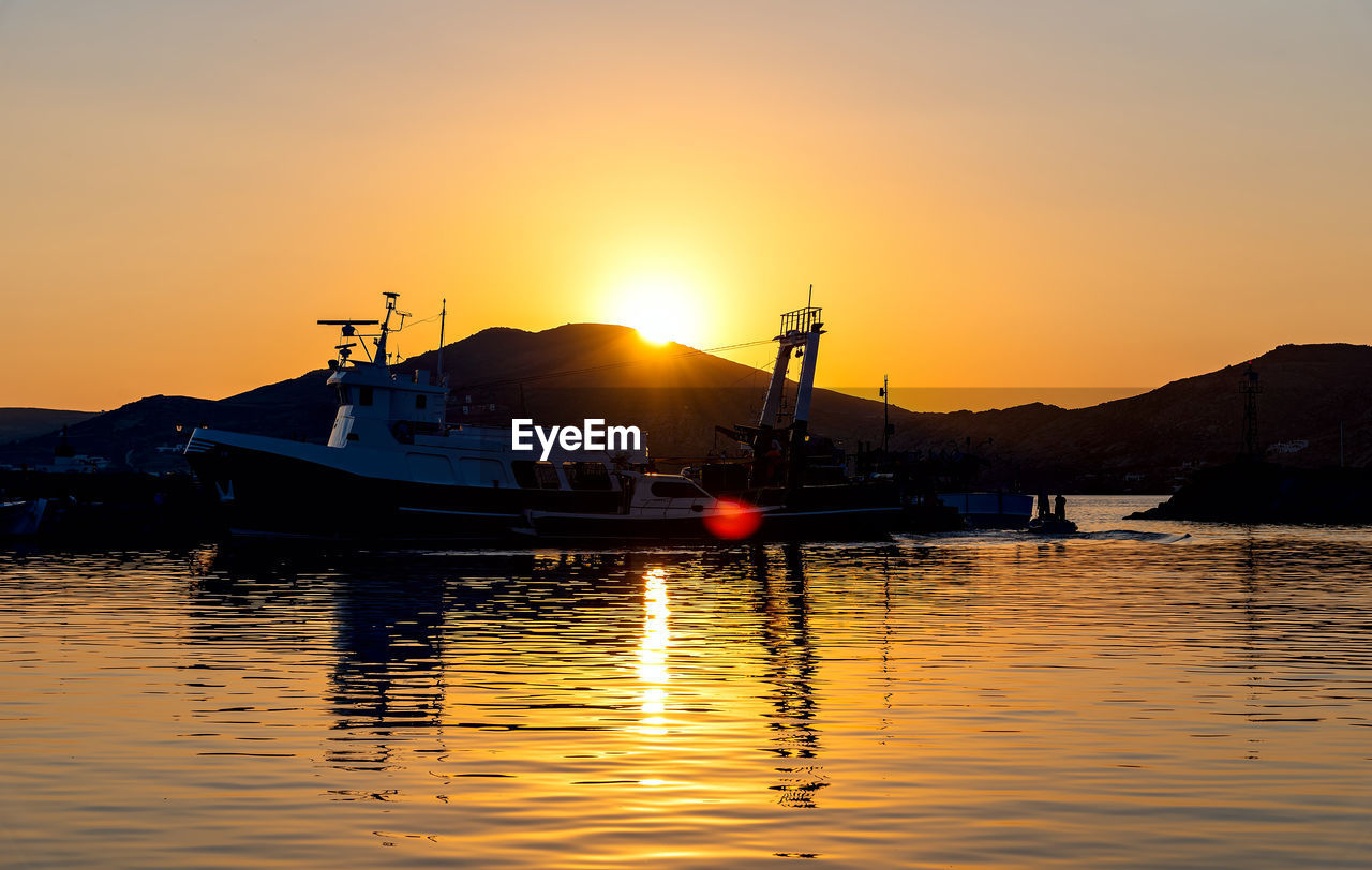 BOATS MOORED IN SEA AGAINST ORANGE SKY