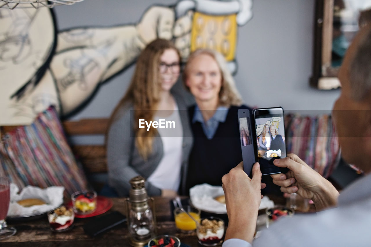 Mature man photographing women through smart phone at restaurant