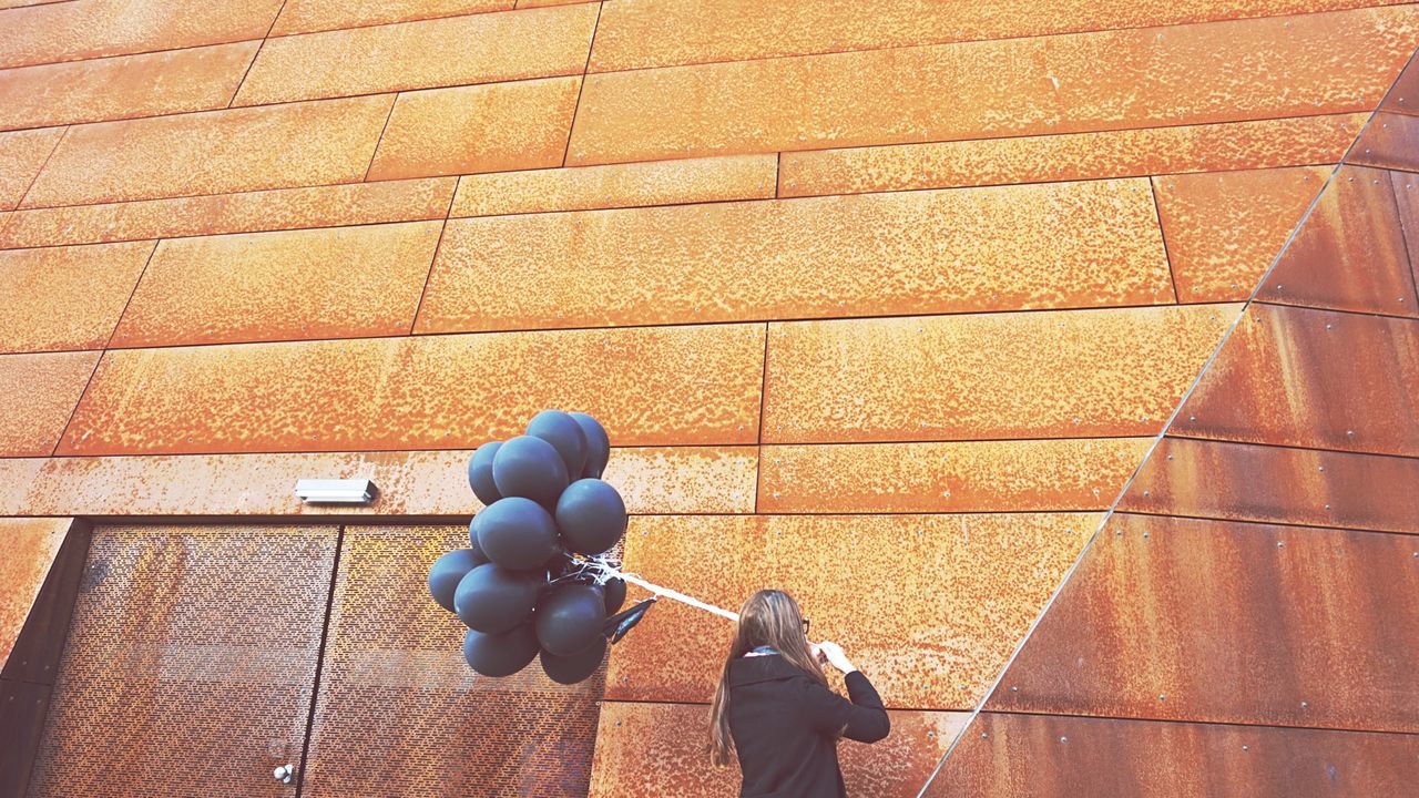 Low angle view of woman with balloons against wall