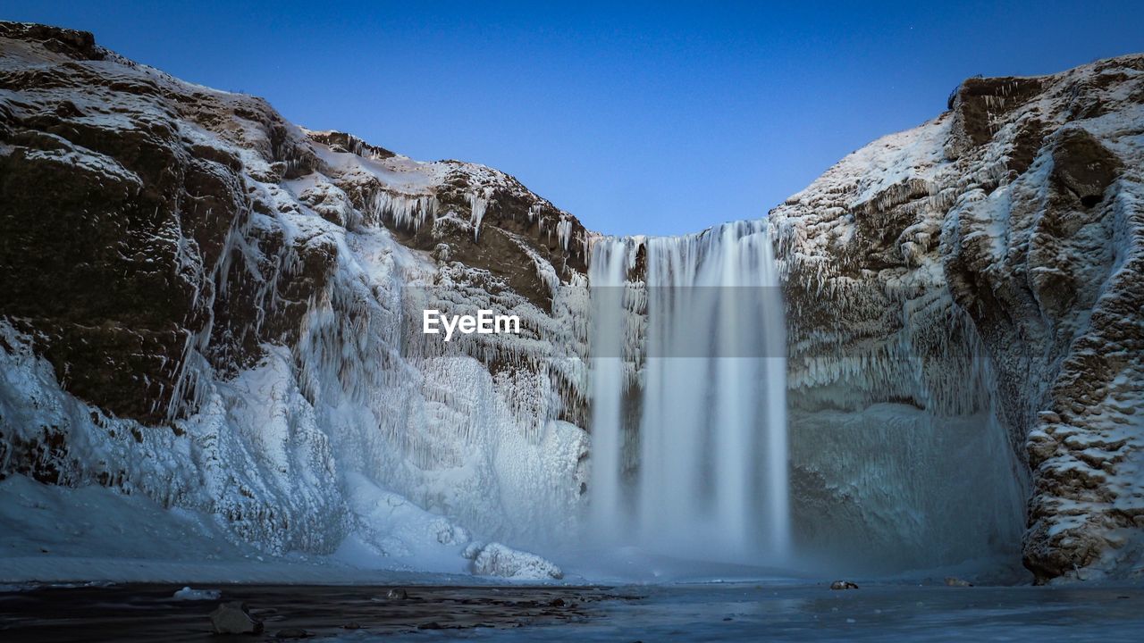 Scenic view of waterfall against clear sky during winter