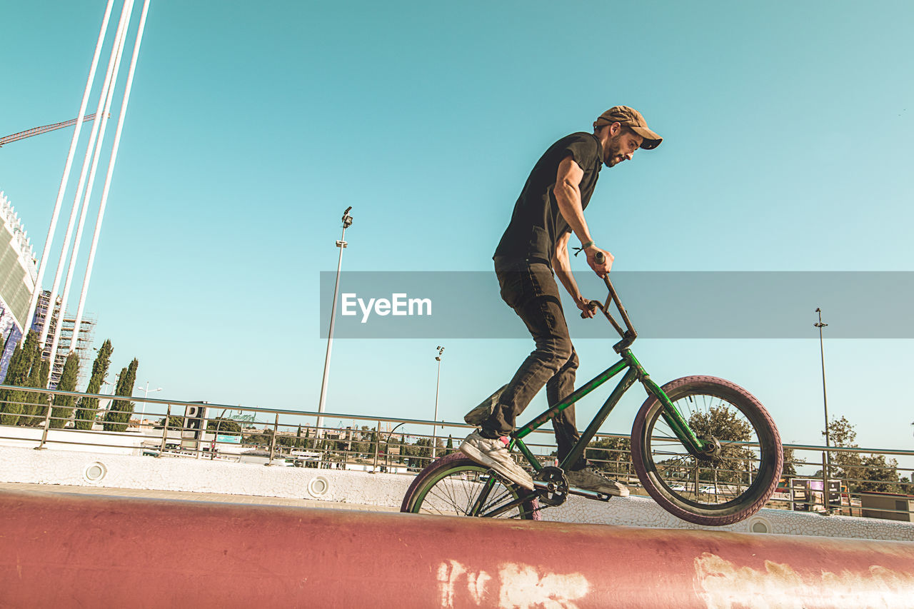 Man riding bicycle on red metallic pipe against sky