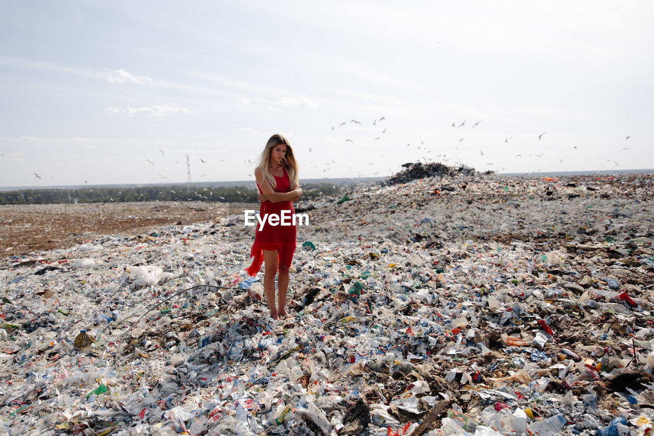 Young woman standing on garbage against sky