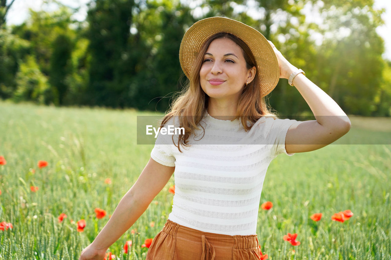 Girl with hat walking in a field with red flowers. summer landscape. warm colors. 