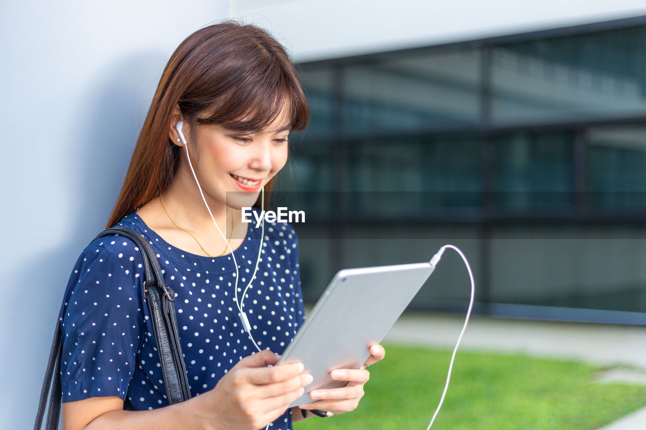 Young attractive asian woman reading the news from a tablet while using earphones to listen to music