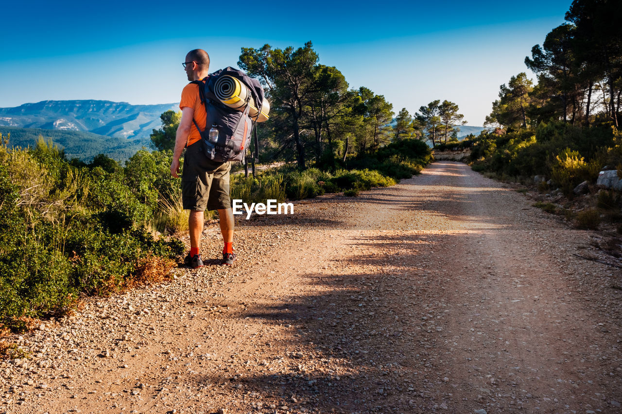 Side view of man with backpack standing on dirt road