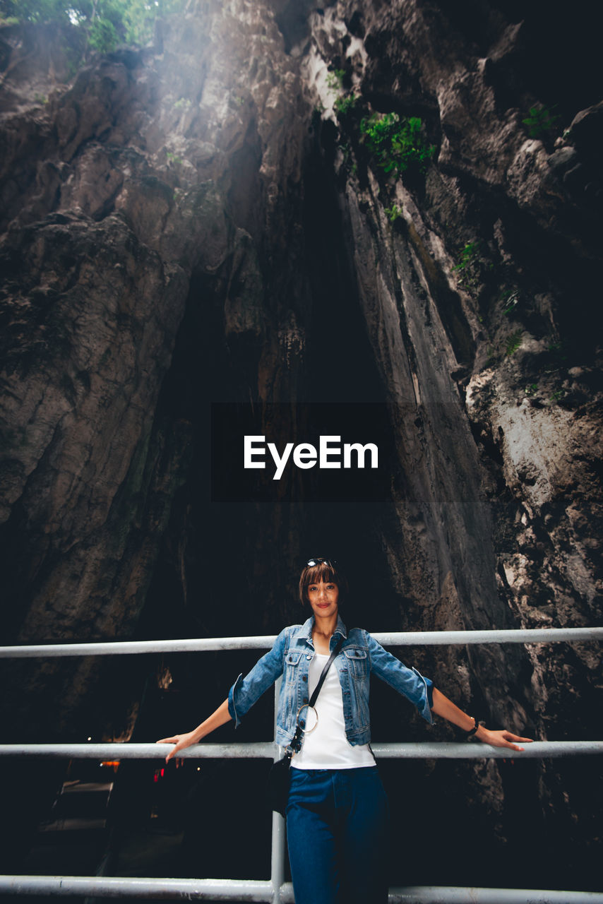 Portrait of young woman standing against rock formation