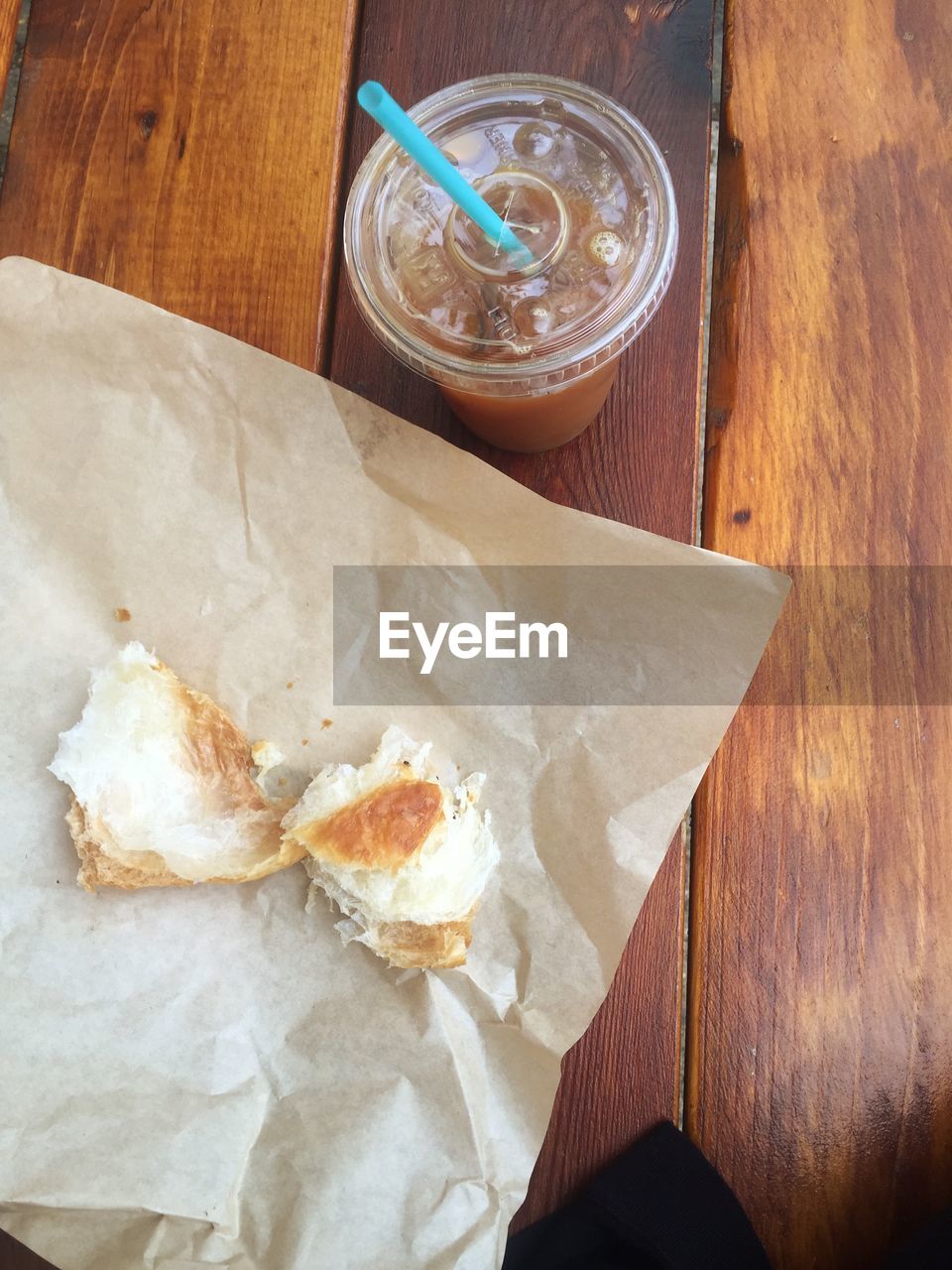 High angle view of leftovers of bread on paper by iced coffee on table