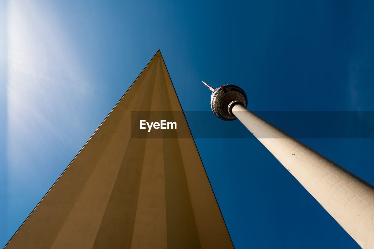 Low angle view of communications tower and building against blue sky