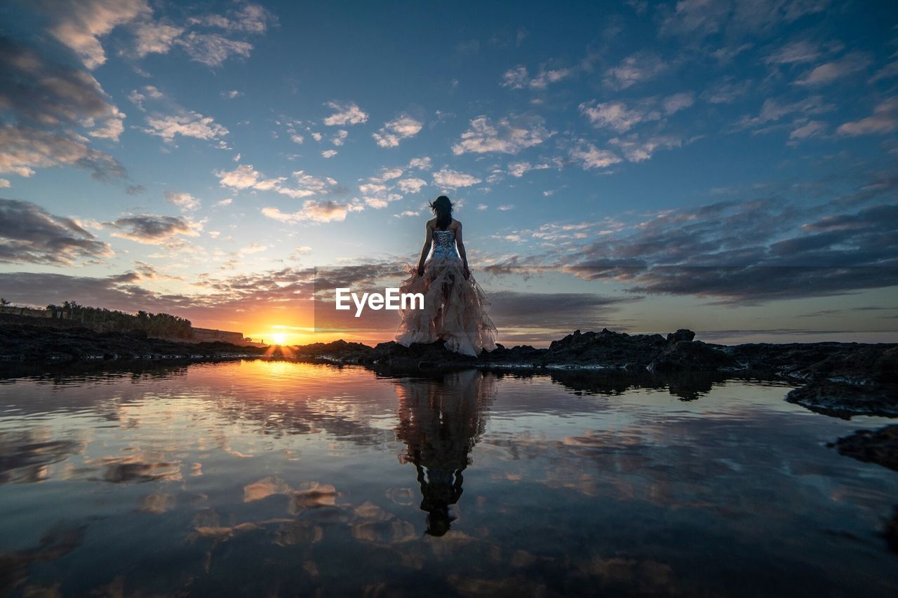 Rear view of woman standing at beach during sunset