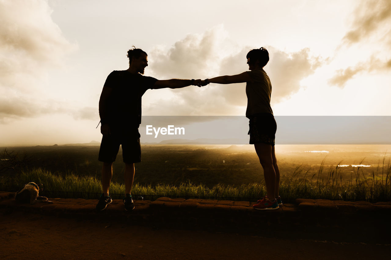 Silhouette couple fist bumping while standing on field against sky