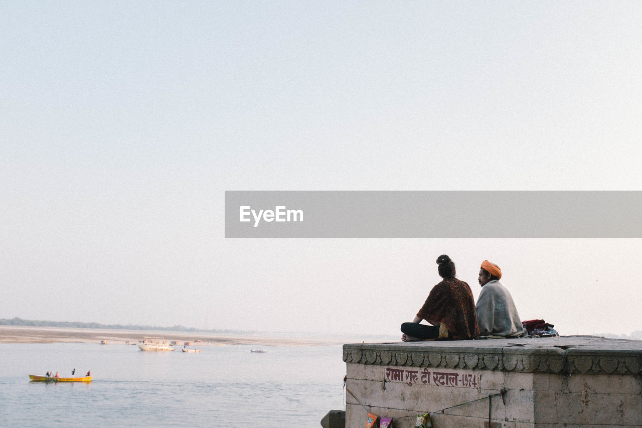 REAR VIEW OF PEOPLE LOOKING AT SEA AGAINST SKY