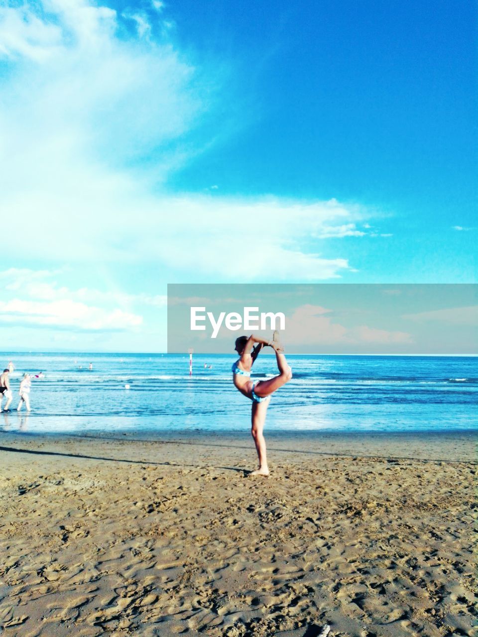 Side view of woman exercising on shore at beach against sky