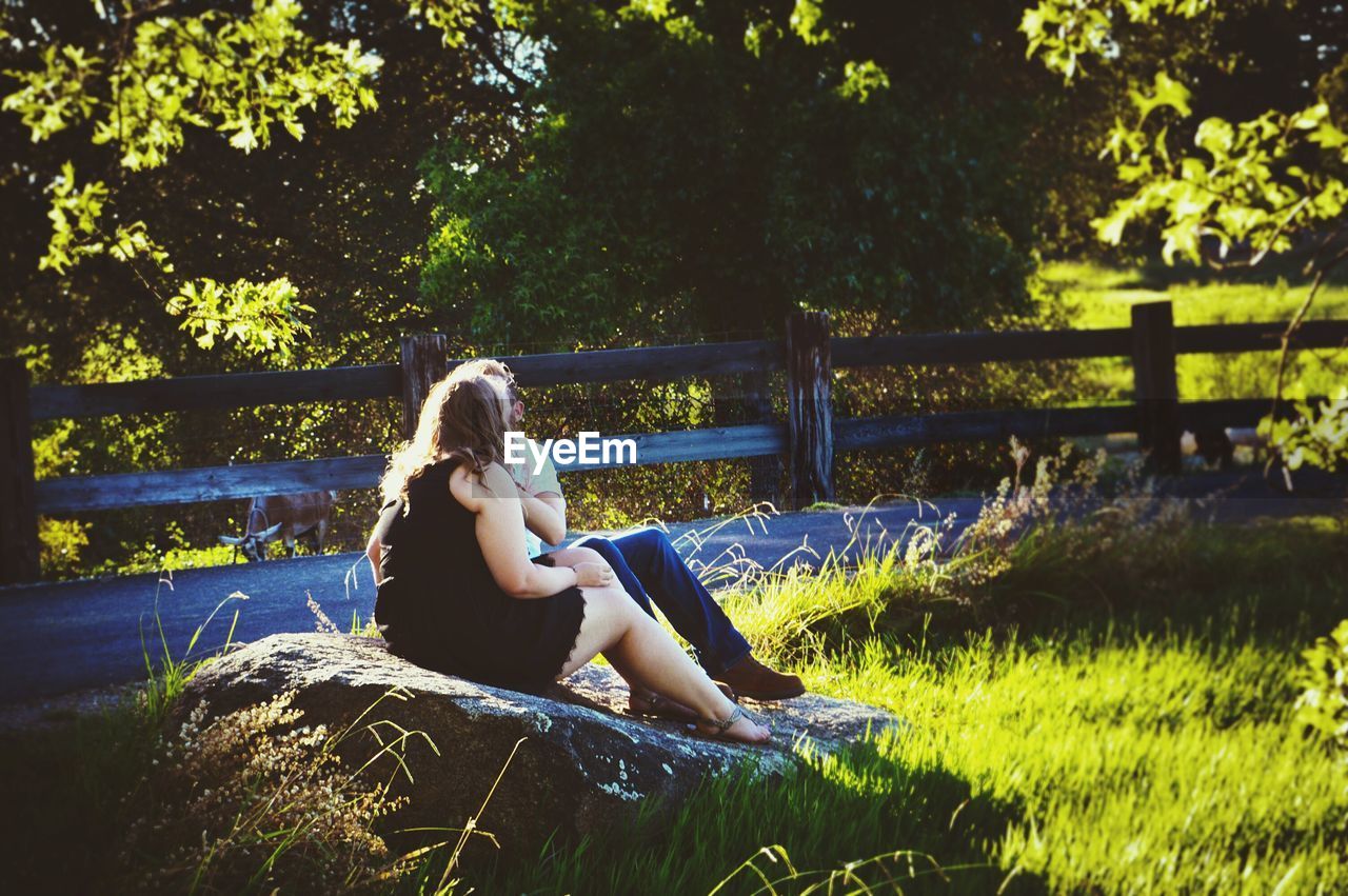 WOMAN SITTING IN GRASS AGAINST TREES