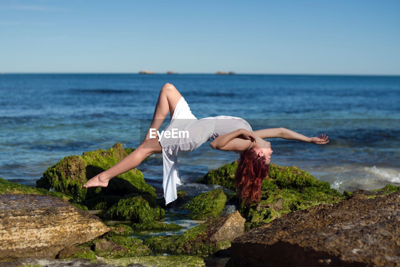 Woman levitating at beach against sky