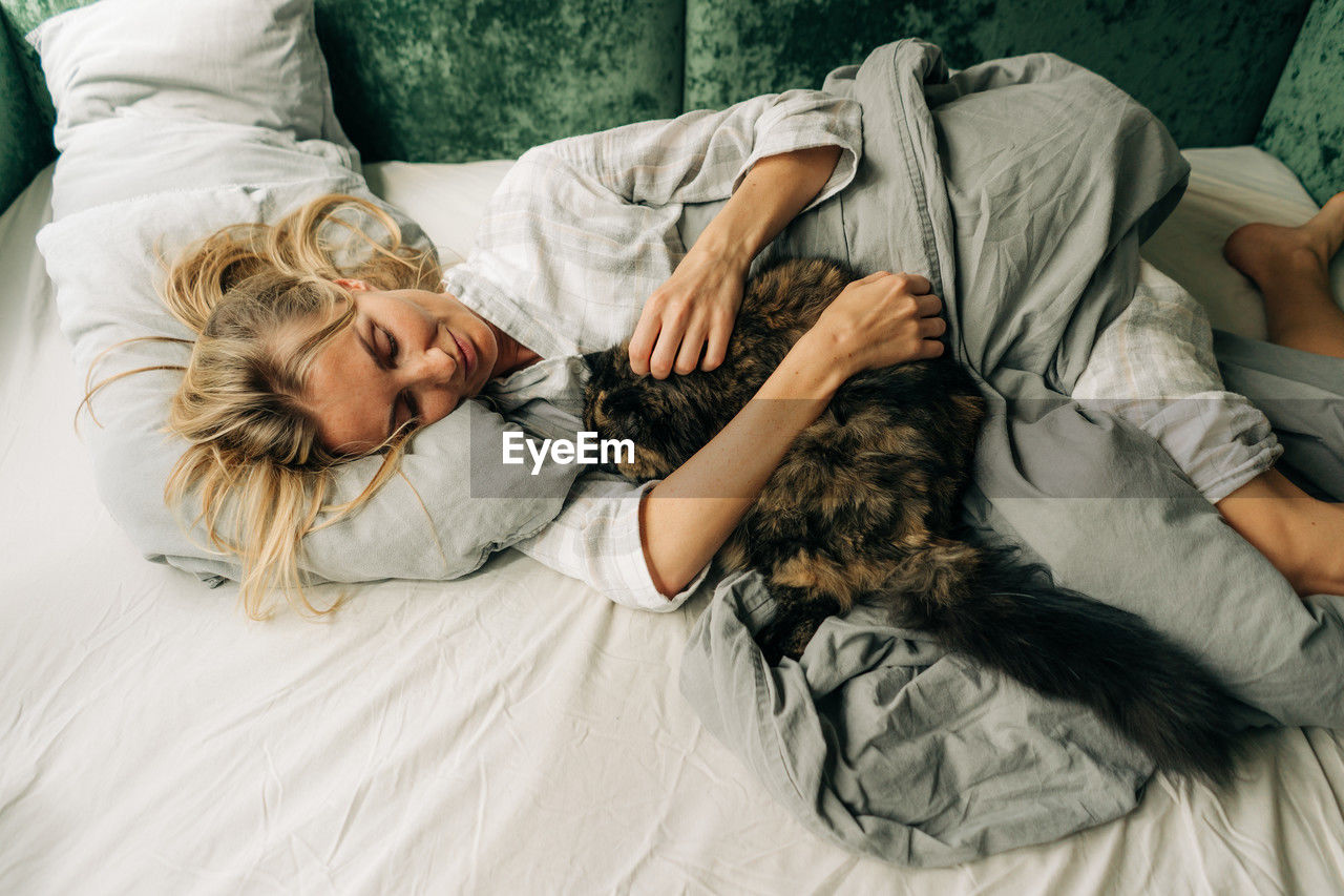 Woman spending morning with her cat lying in bed after waking up.