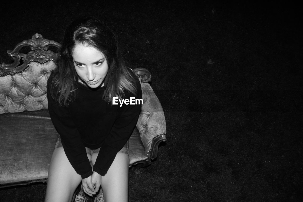 High angle view of thoughtful young woman looking away while sitting on couch outdoors at night