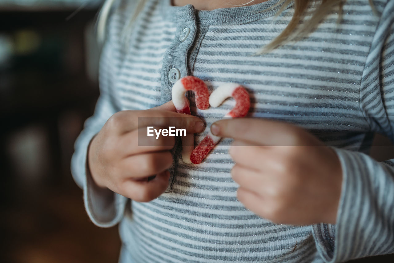 Cropped hands of girl holding candy canes in a heart on her chest