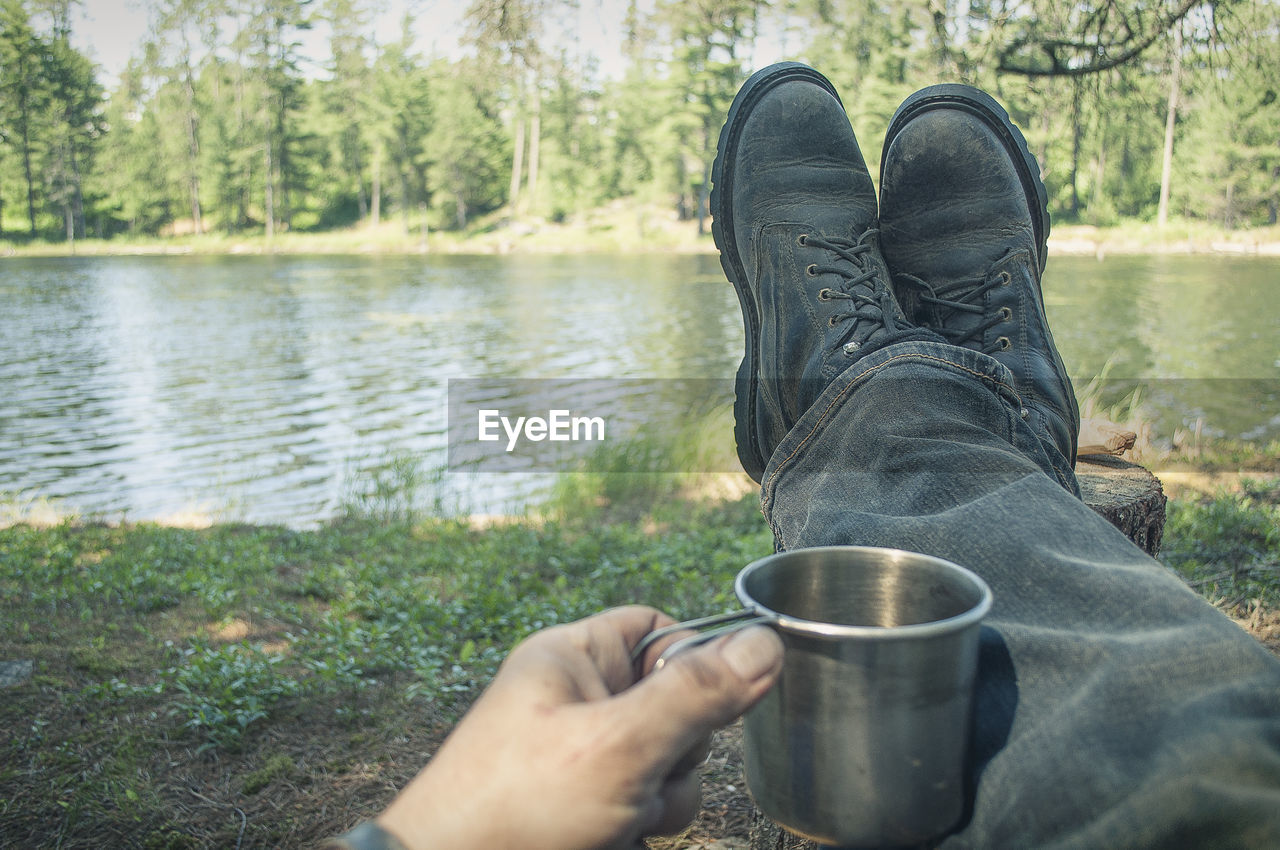 Low section of man with coffee lying at lakeshore