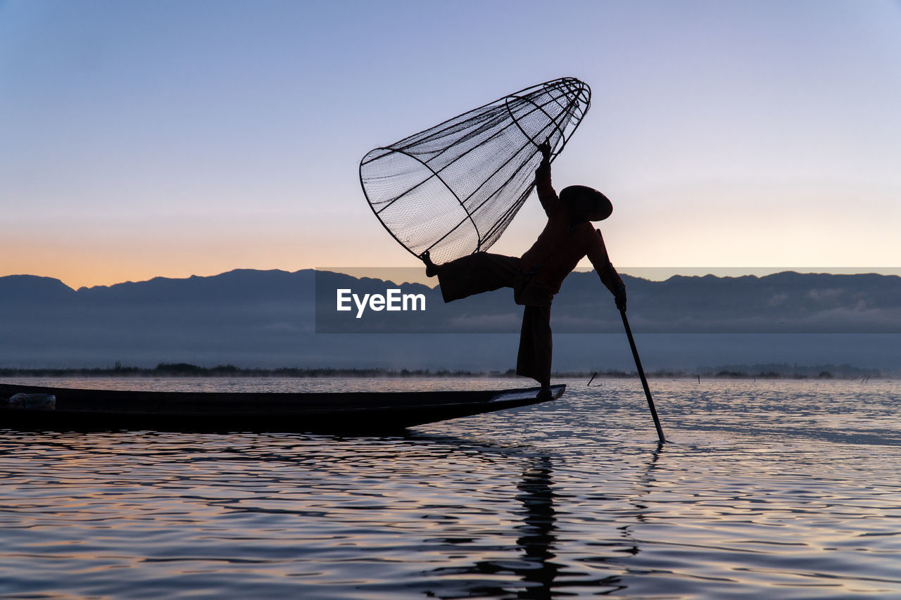 Silhouette of traditional fisherman with boat on inle lake during sunrise against sky