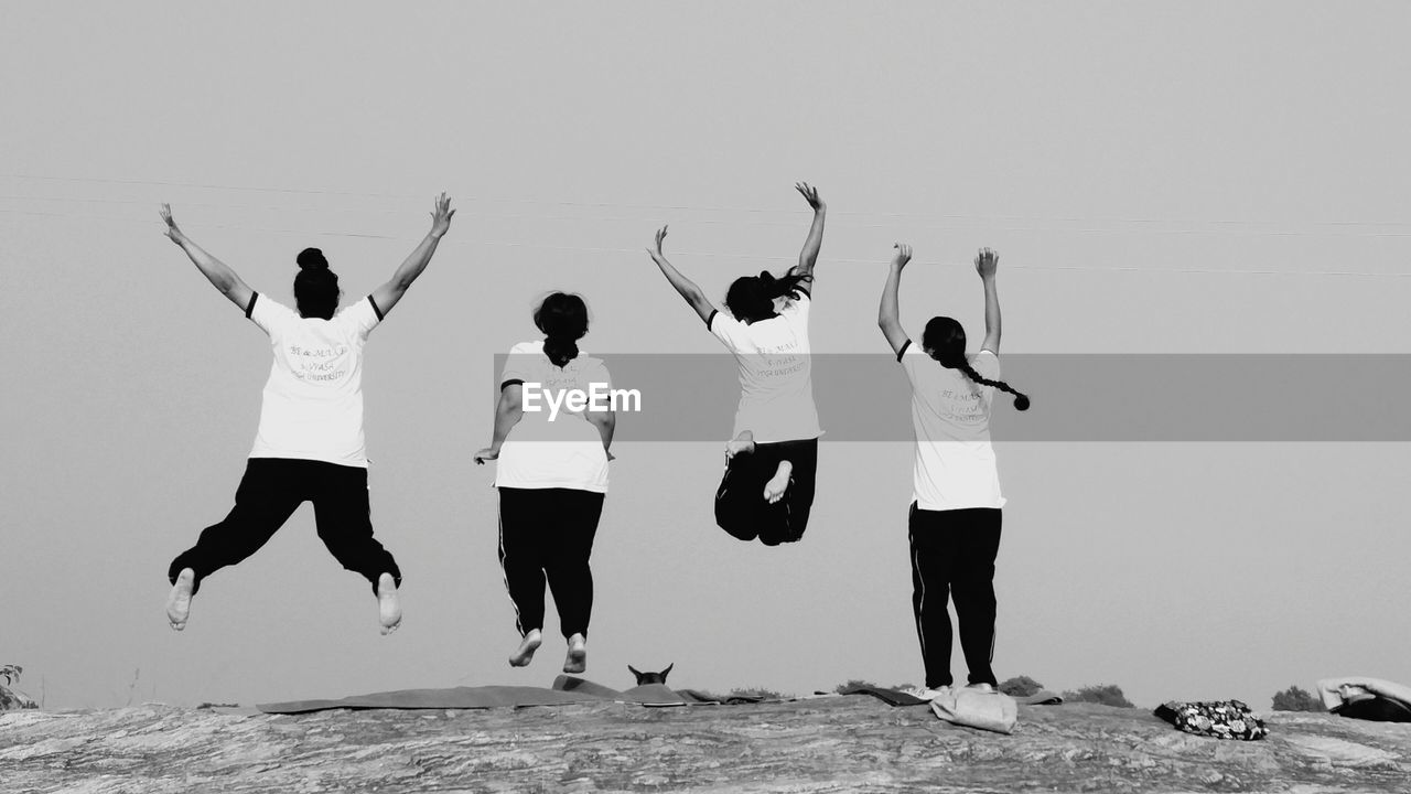 Rear view of friends jumping on rock against clear sky at beach