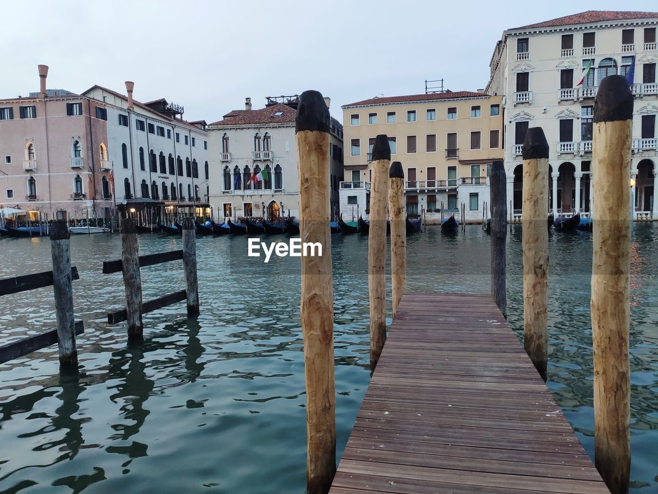 Wooden posts in canal amidst buildings against sky