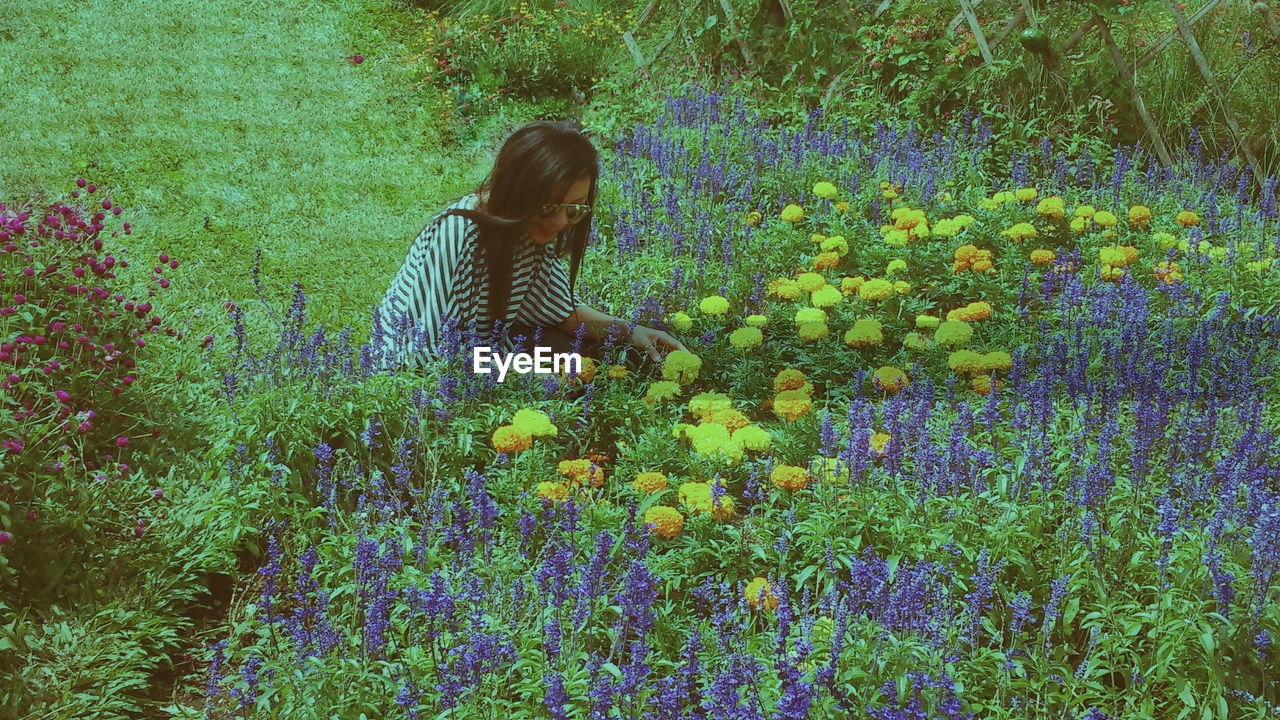 Smiling woman crouching by flowers blooming on field