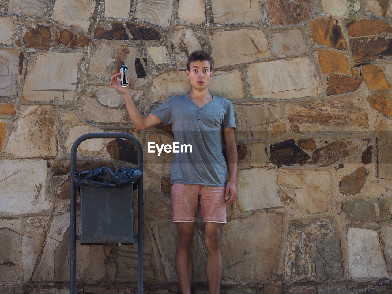 Portrait of surprised young man holding can against wall