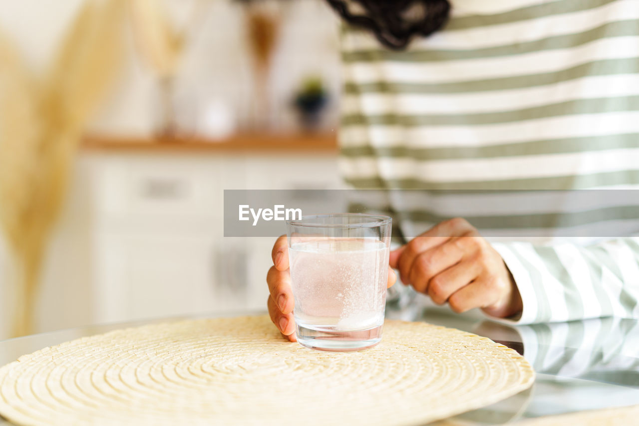 Dissolving fizz drug in glass of water. unrecognizable female taking medicine at home