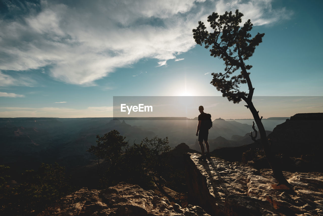 SILHOUETTE MAN STANDING ON ROCKS AGAINST SKY