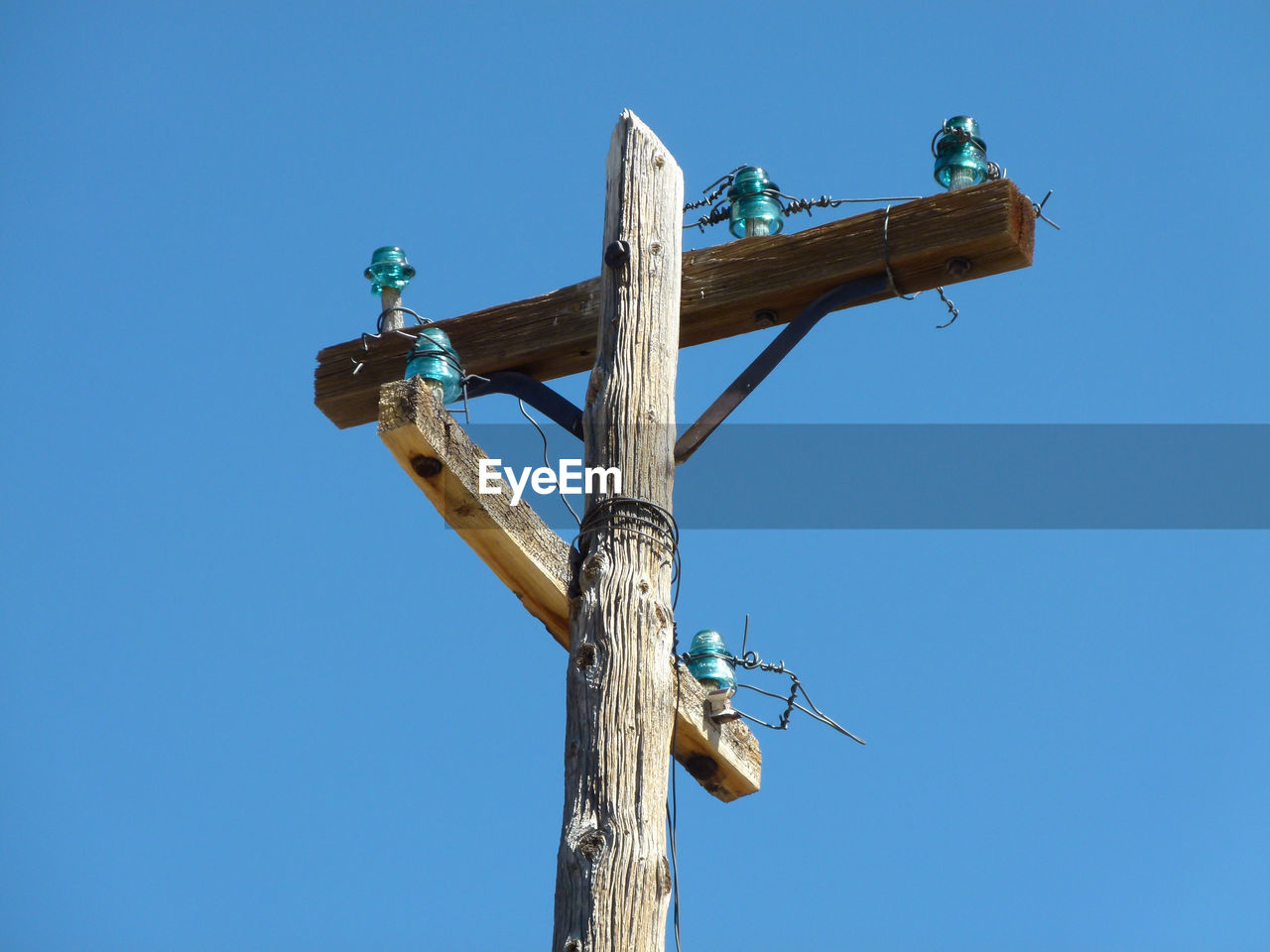 Low angle view of telephone pole against clear blue sky