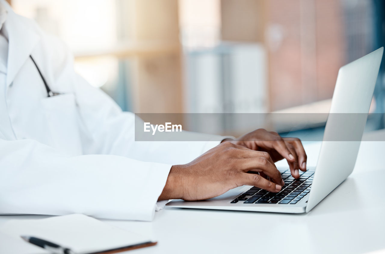 midsection of doctor using laptop at desk in office