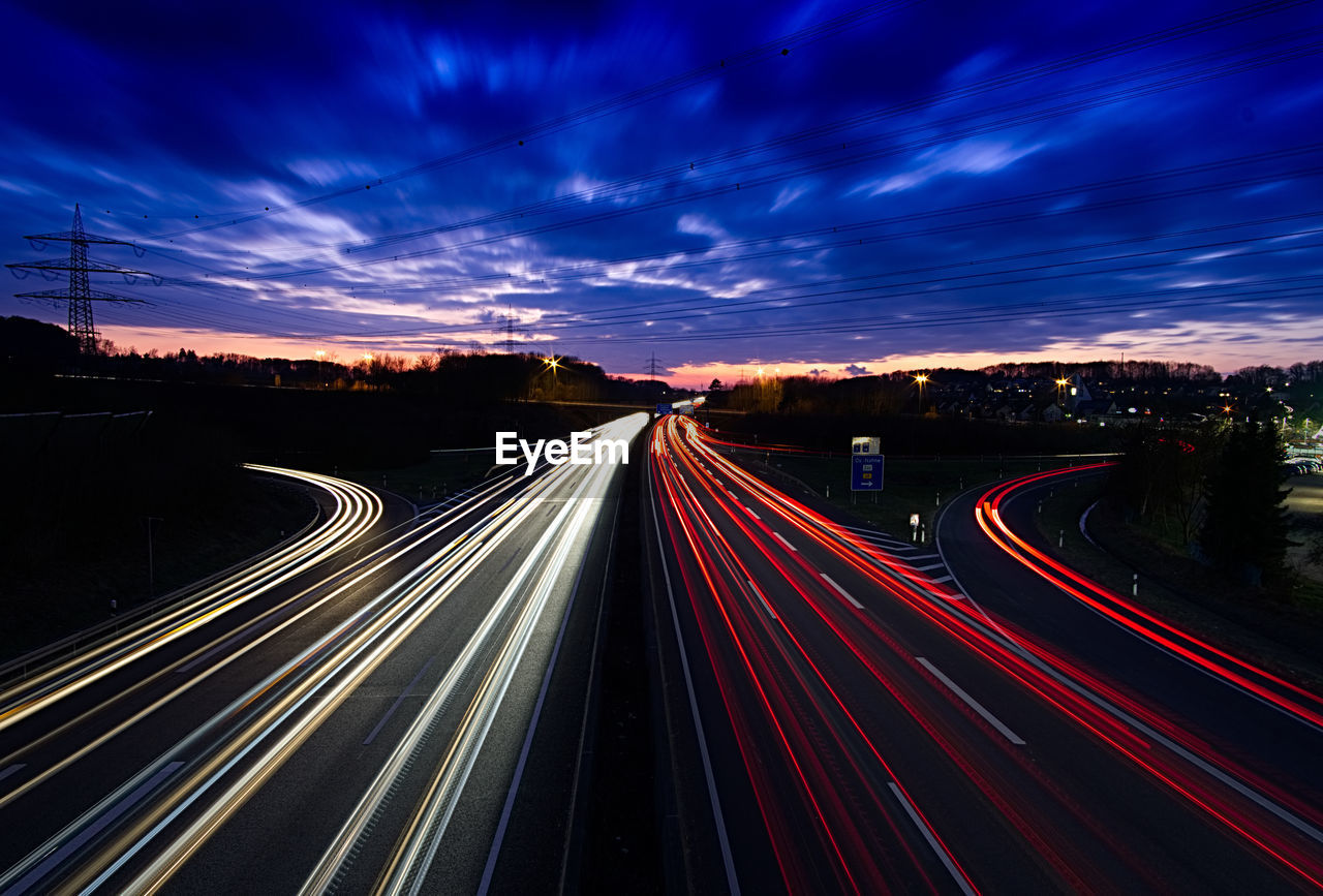 Light trails on road against dramatic sky at night