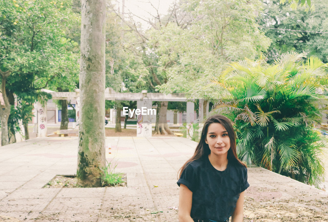 Portrait of young woman against trees at park