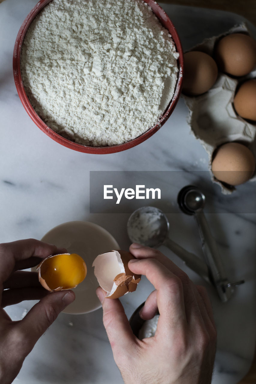 High angle view of hand holding egg over bowl