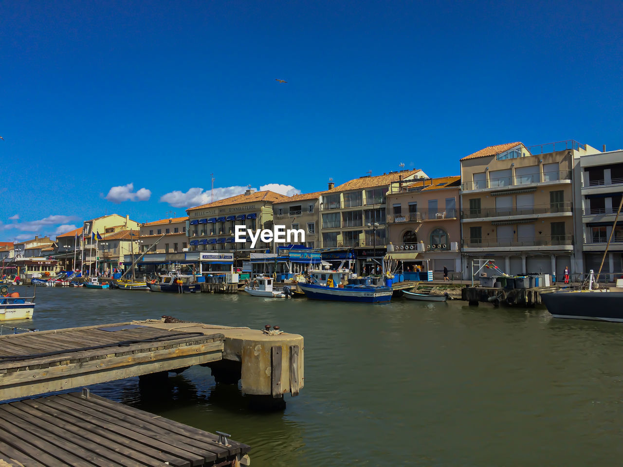 BOATS MOORED IN CANAL BY BUILDINGS AGAINST BLUE SKY