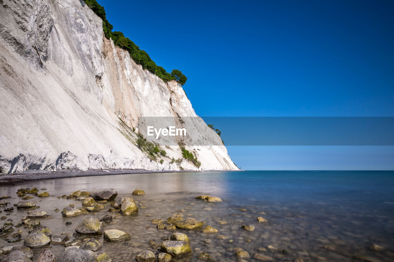 SCENIC VIEW OF SEA AND ROCKS AGAINST CLEAR BLUE SKY