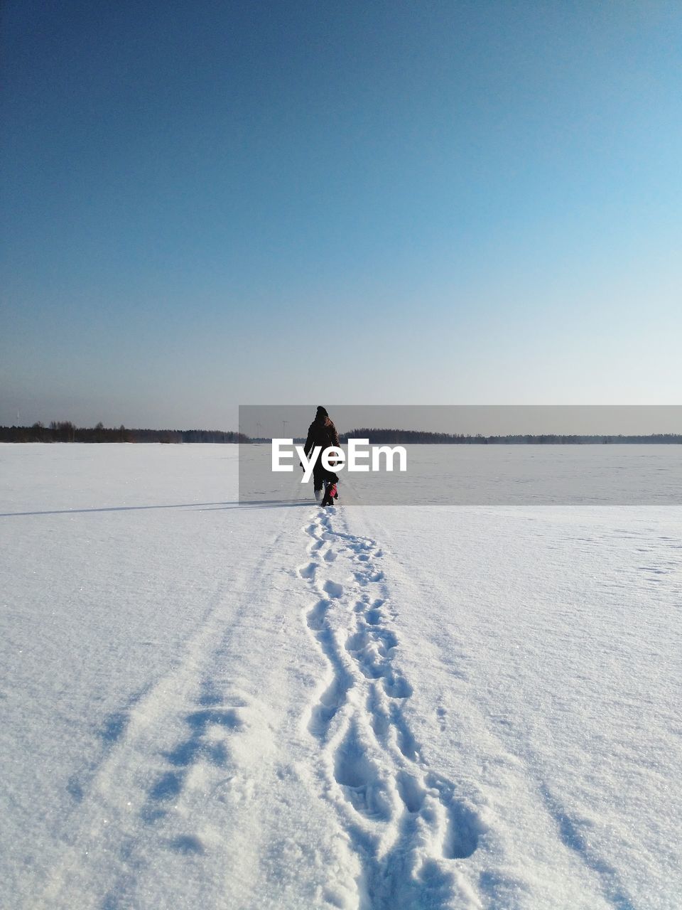 Full length of woman with dog walking on snowy field against clear sky