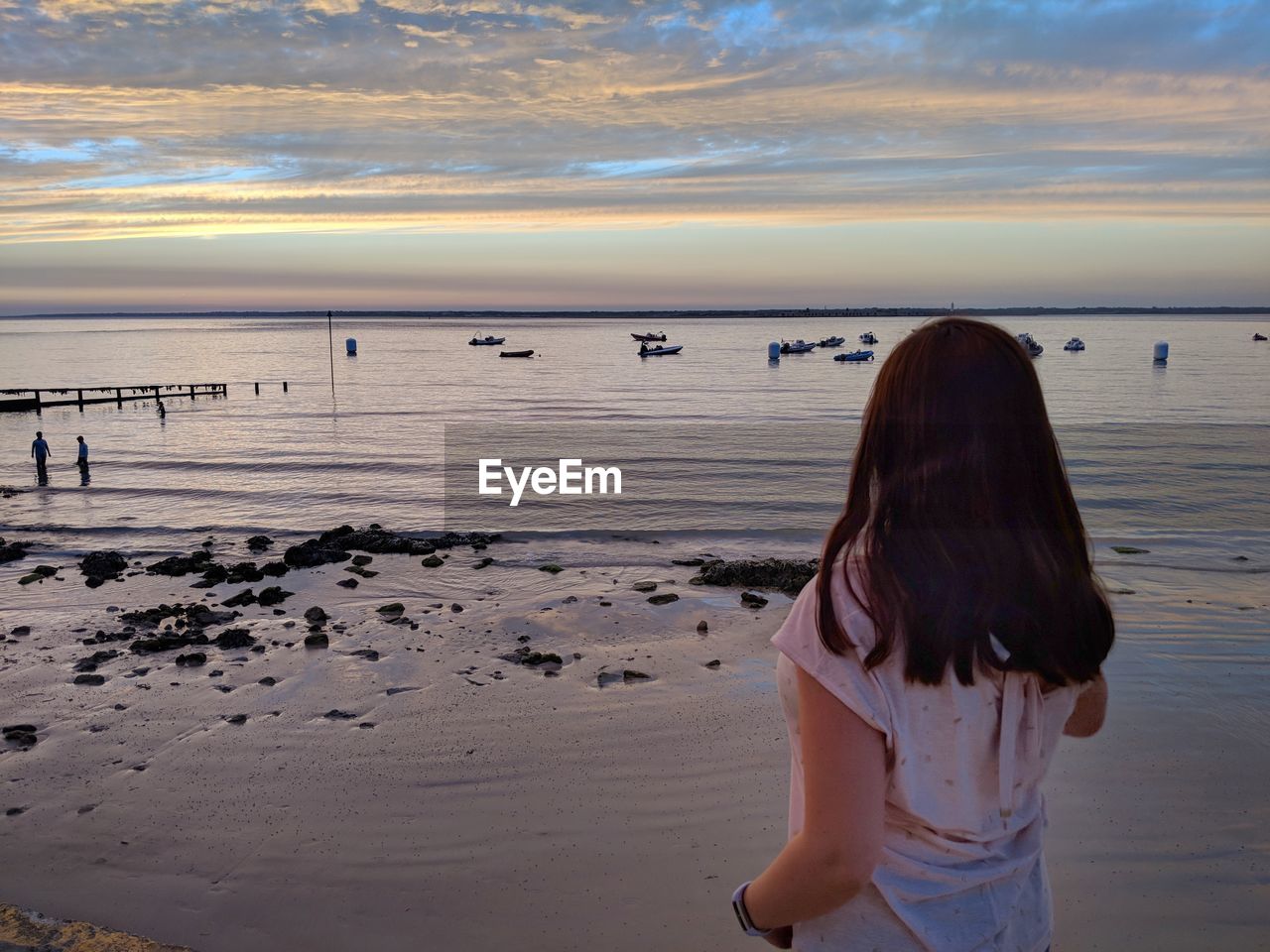 Rear view of woman standing at beach against sky during sunset