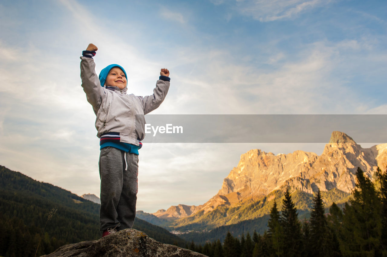 Low angle view of boy standing on mountain against sky