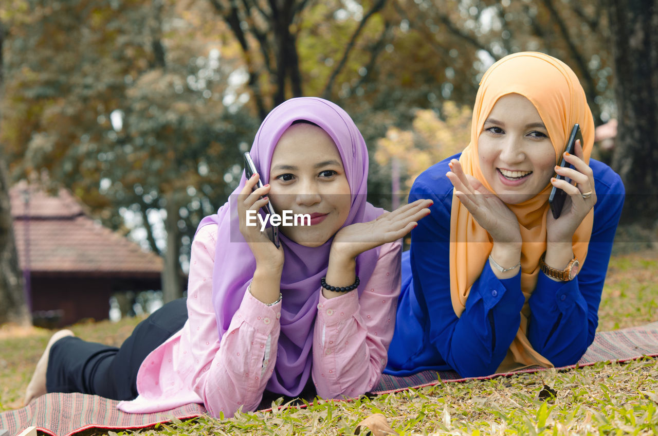 Friendship and happiness concept. portrait of smile young muslimah laying on grass at city park