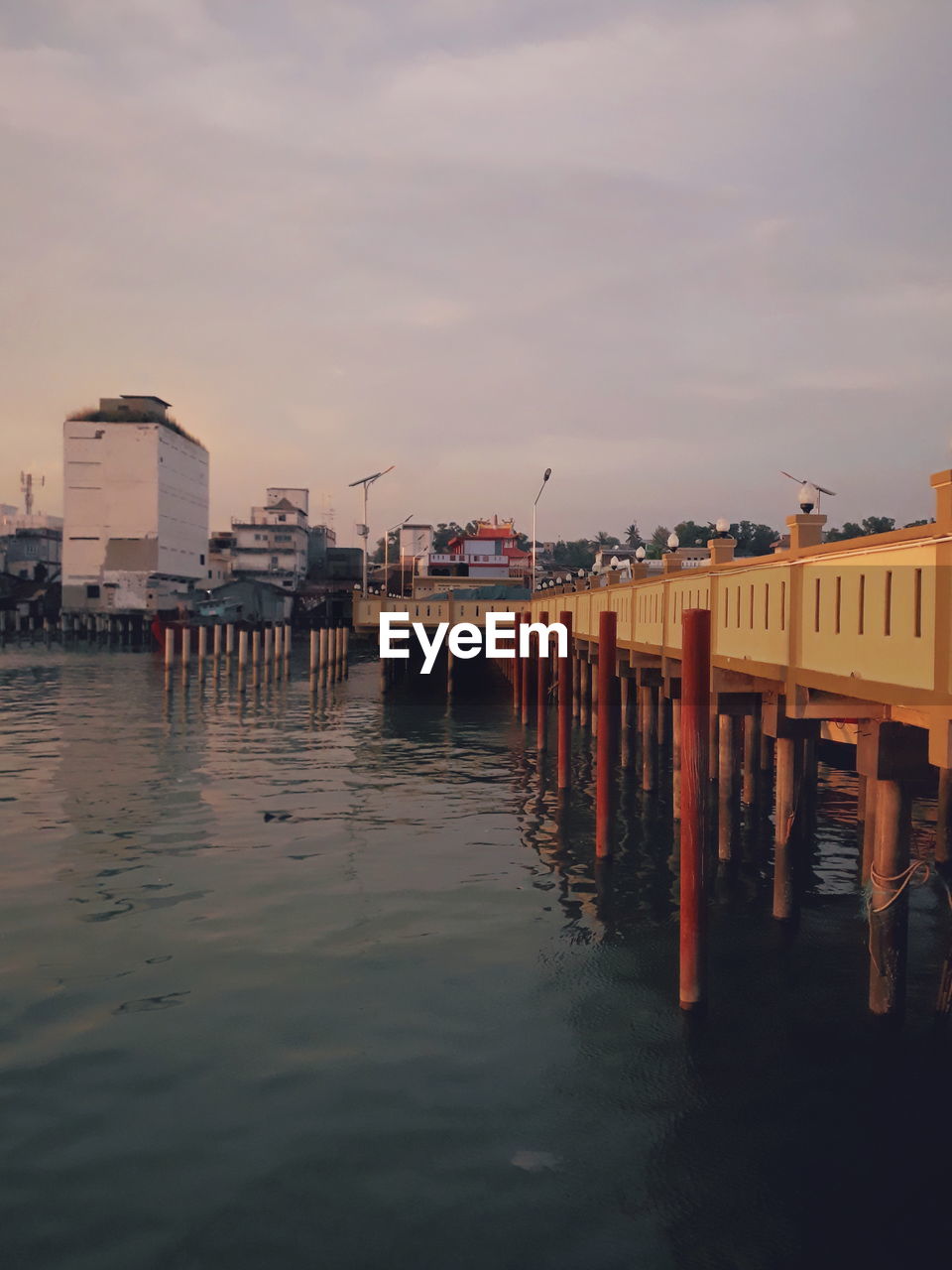 Pier on sea by buildings against sky during sunset